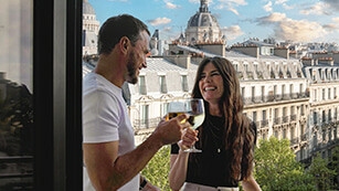 Un couple trinque sur un balcon d’hôtel avec vue sur la ville – profite toi-même de ce confort avec nos hôtels près du Hungaroring, billets F1 et transferts inclus