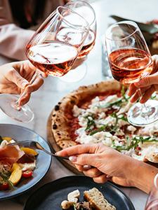 Brindis compartido con pizza y platos de temporada durante una comida animada en grupo.