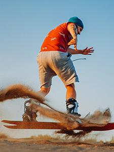 Persona deslizándose por una duna en sandboard durante una salida organizada llena de adrenalina.